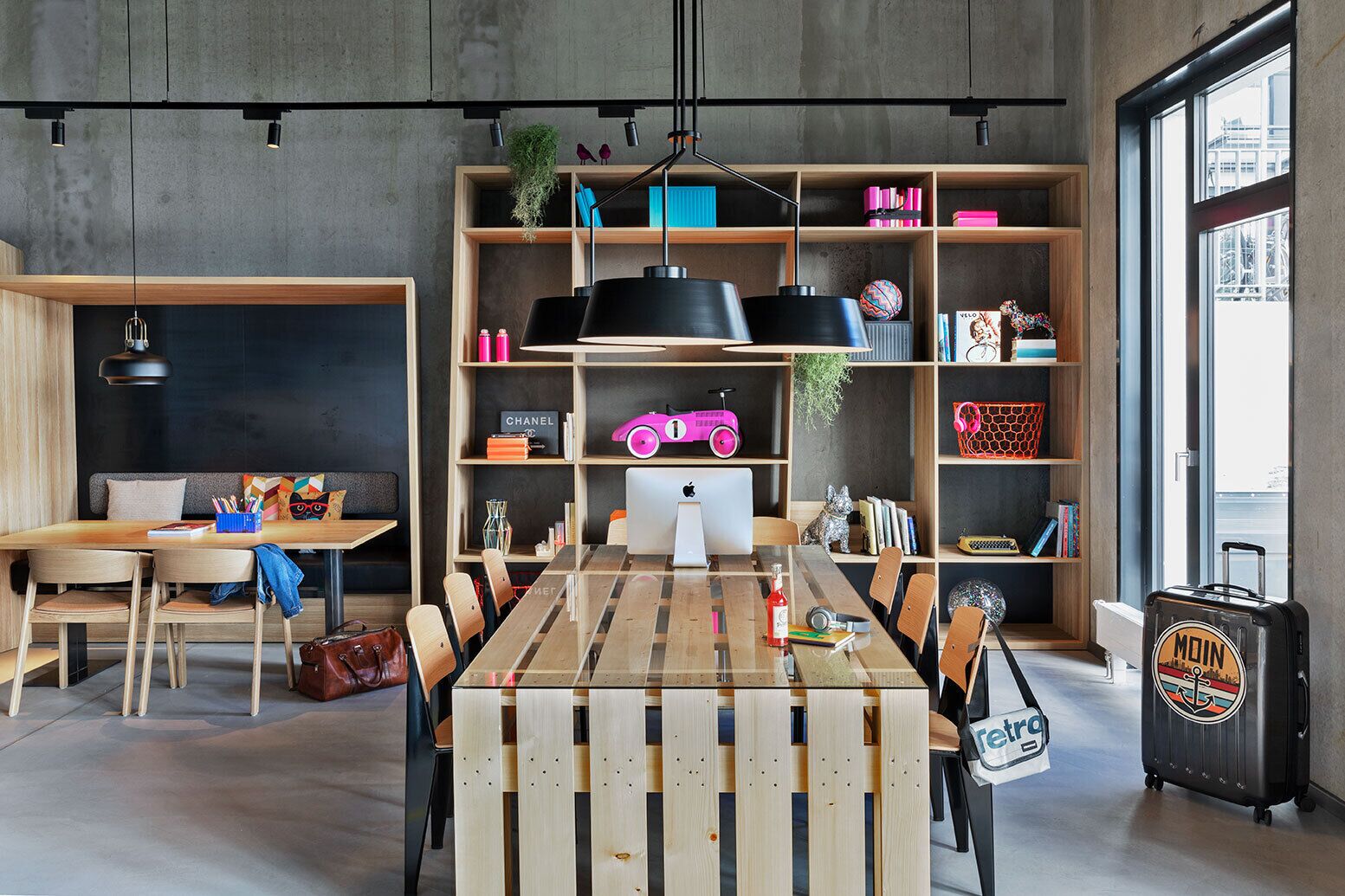 Un interior moderno con una mesa de comedor de madera, sillas, una estantería y una maleta.