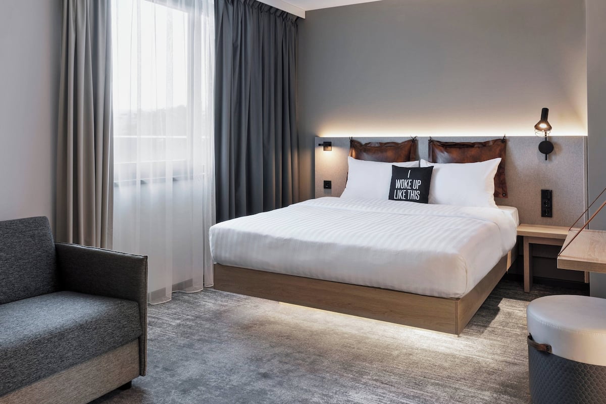 A modern hotel room with a large bed, a sofa, a desk, and a lamp.
