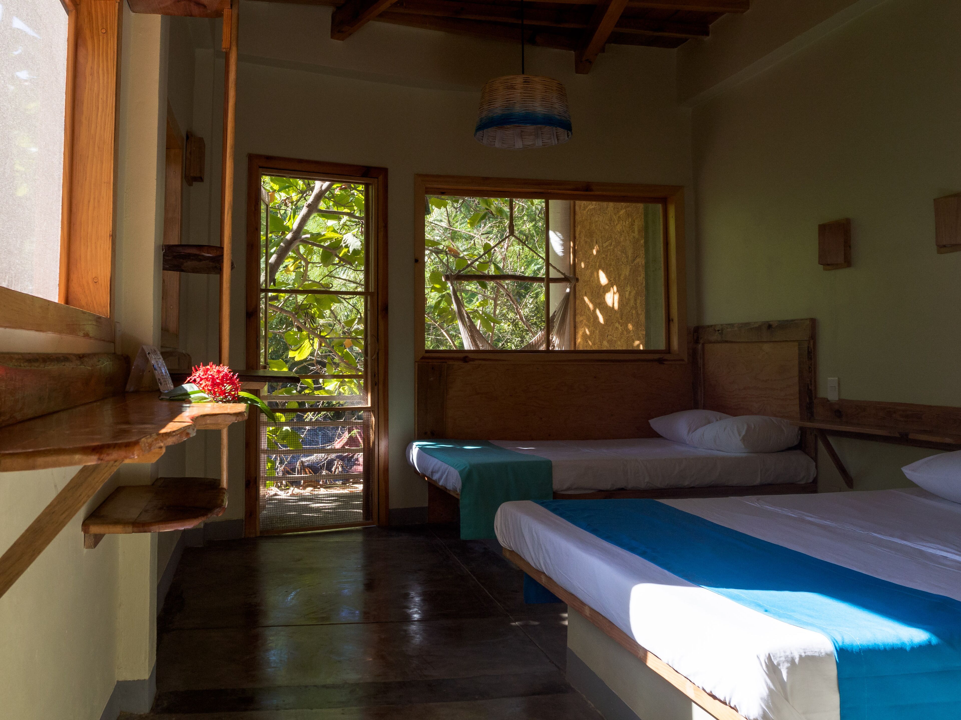 A room with two beds, a wooden bench, a small table, and a hanging light fixture.