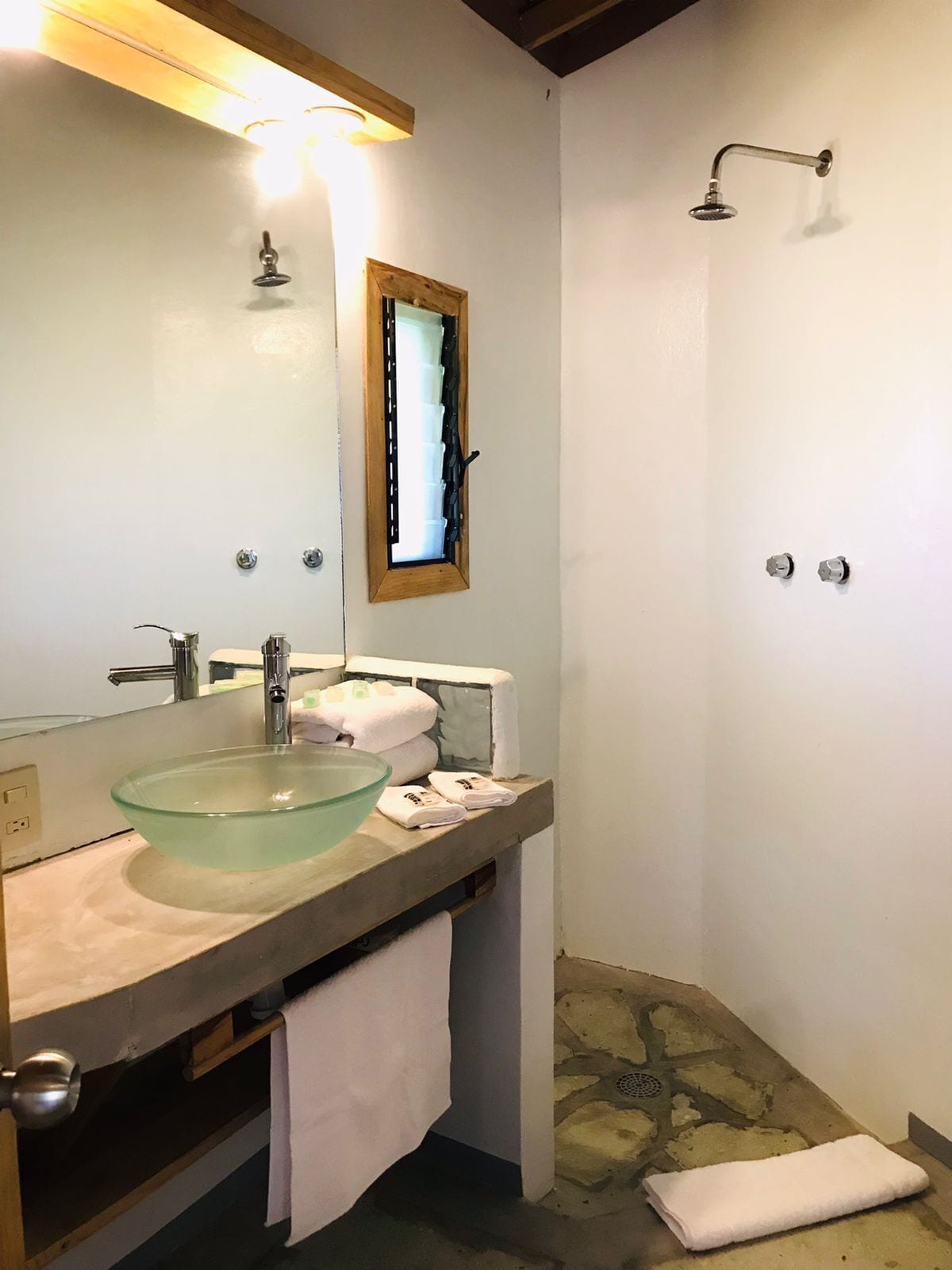 Ein Badezimmer mit einem Glaswaschbecken, einer Holzausstattung, einem Spiegel, einer Dusche und einem Steinboden.