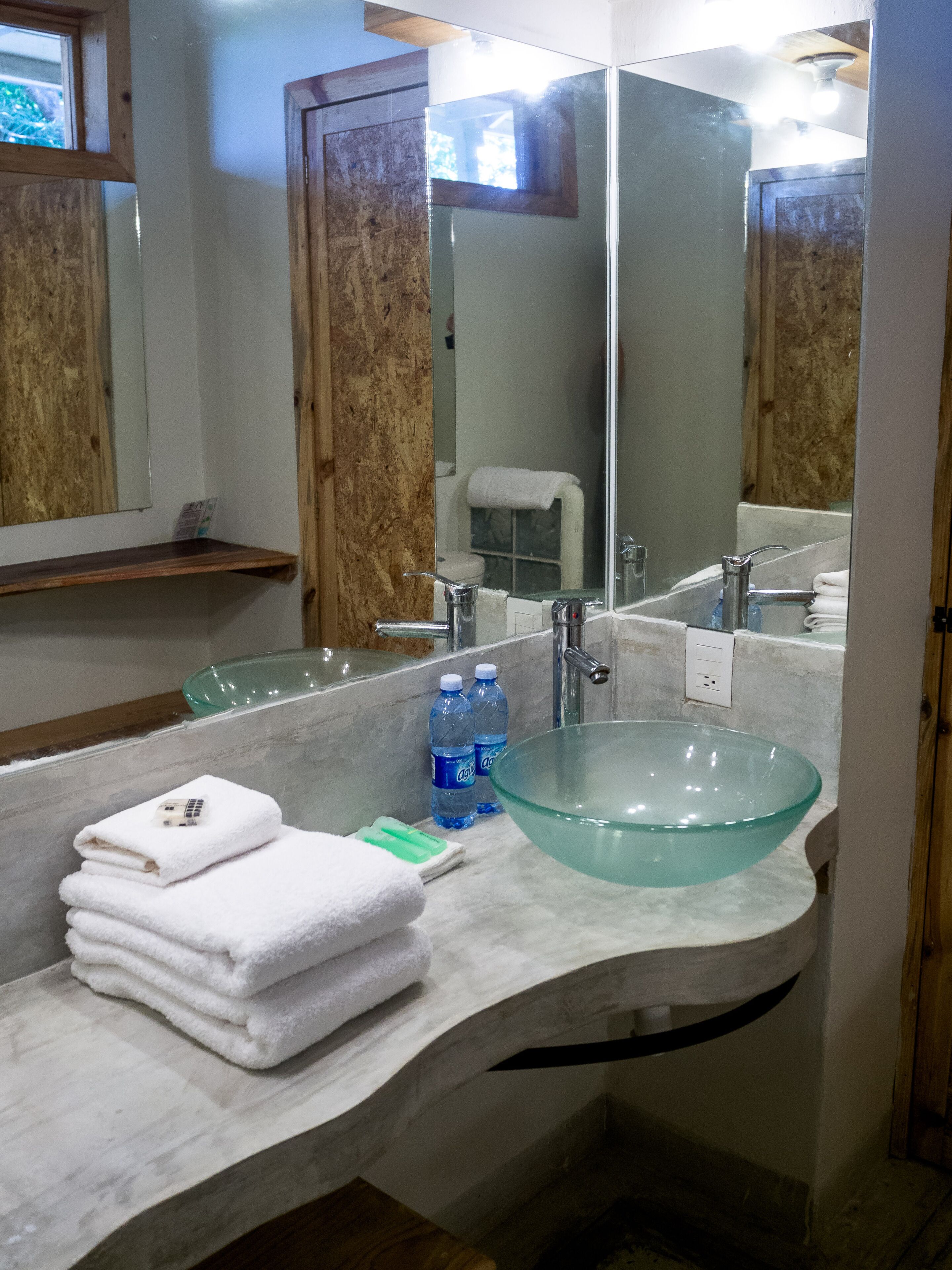 A bathroom with a glass bowl sink, white towels, and two bottles of water.