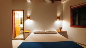 Un dormitorio con una cama, dos mesitas de noche, una ventana y una puerta que da a otra habitación.