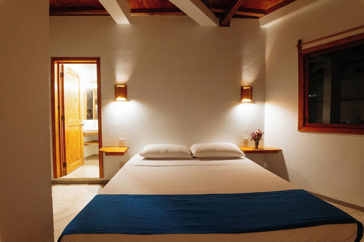 A bedroom with a bed, two bedside tables, a window, and a door leading to another room.