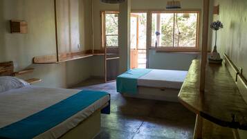 A room with two beds, a wooden bench, a small table, and a window with a view of greenery.