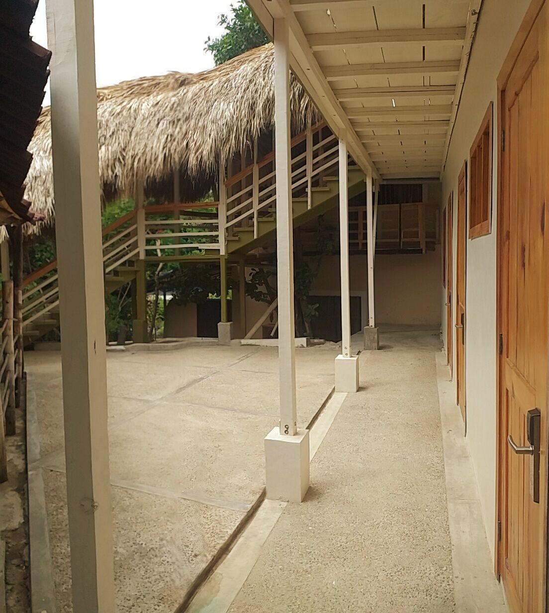 A covered outdoor area with a concrete floor, wooden doors, and a thatched roof structure.