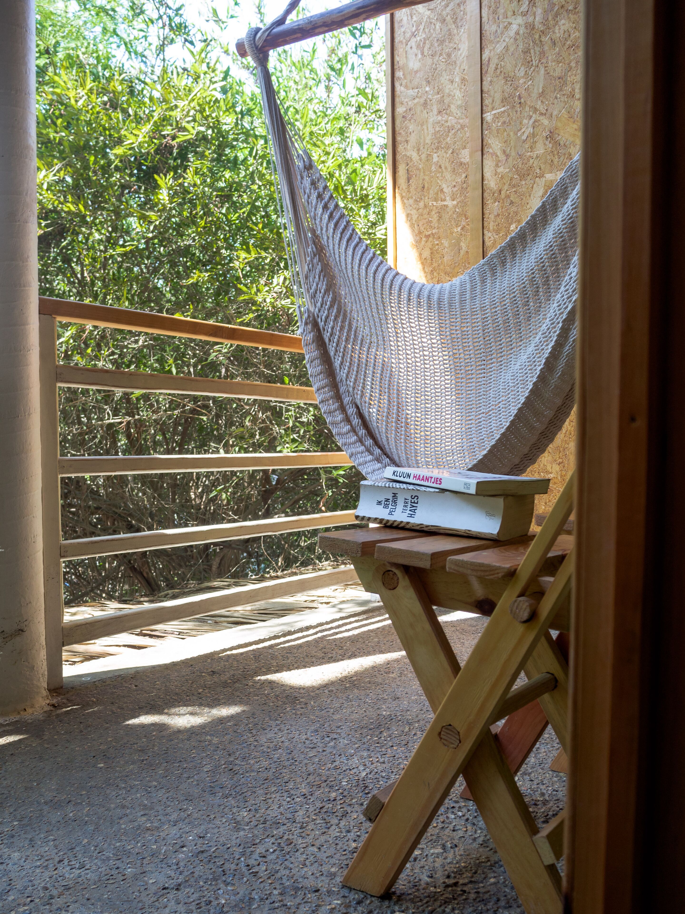 A hammock chair with a book, wooden deck, and a view of greenery.