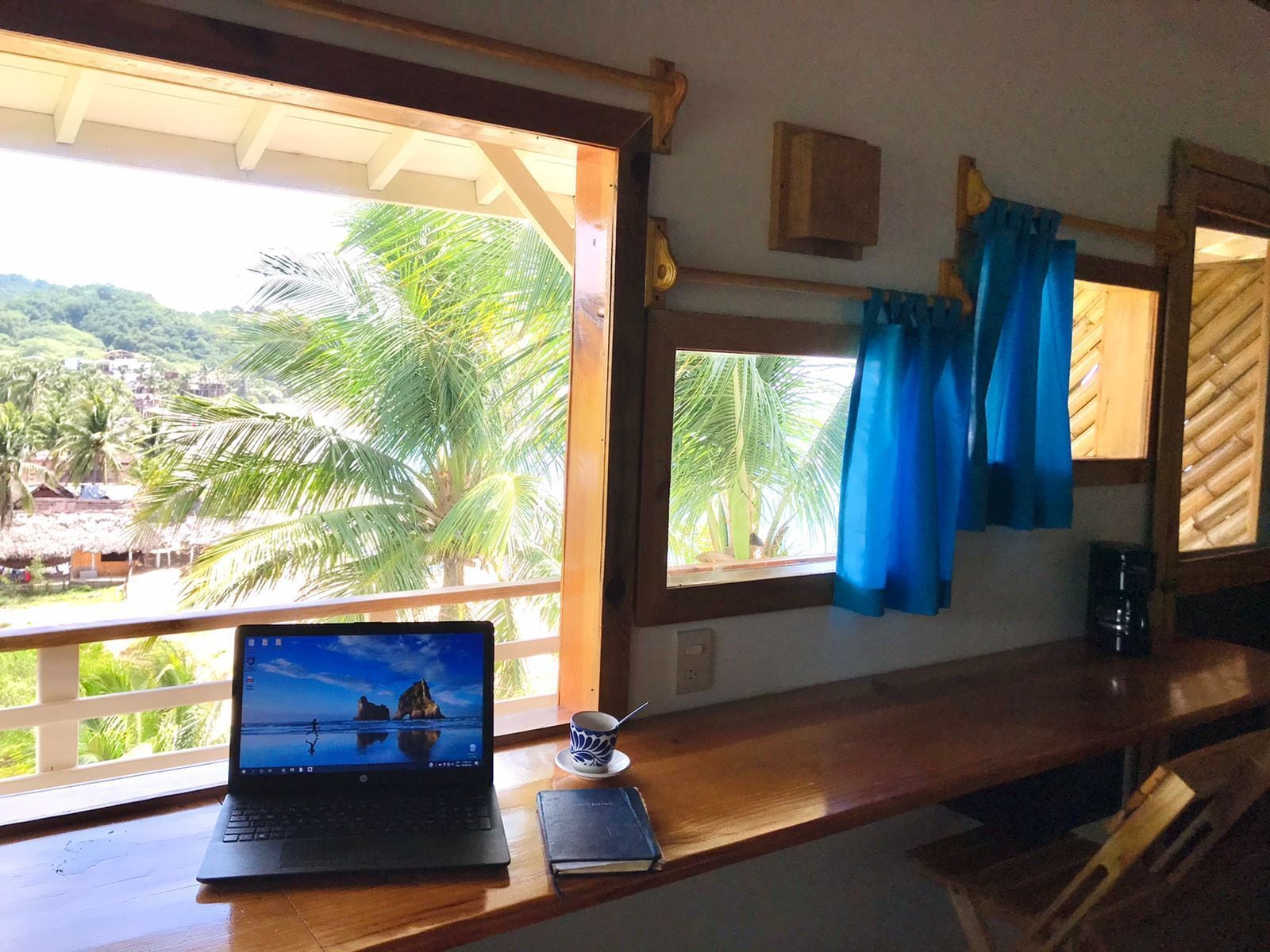 Una laptop sobre un escritorio de madera con vista a palmeras y una playa.