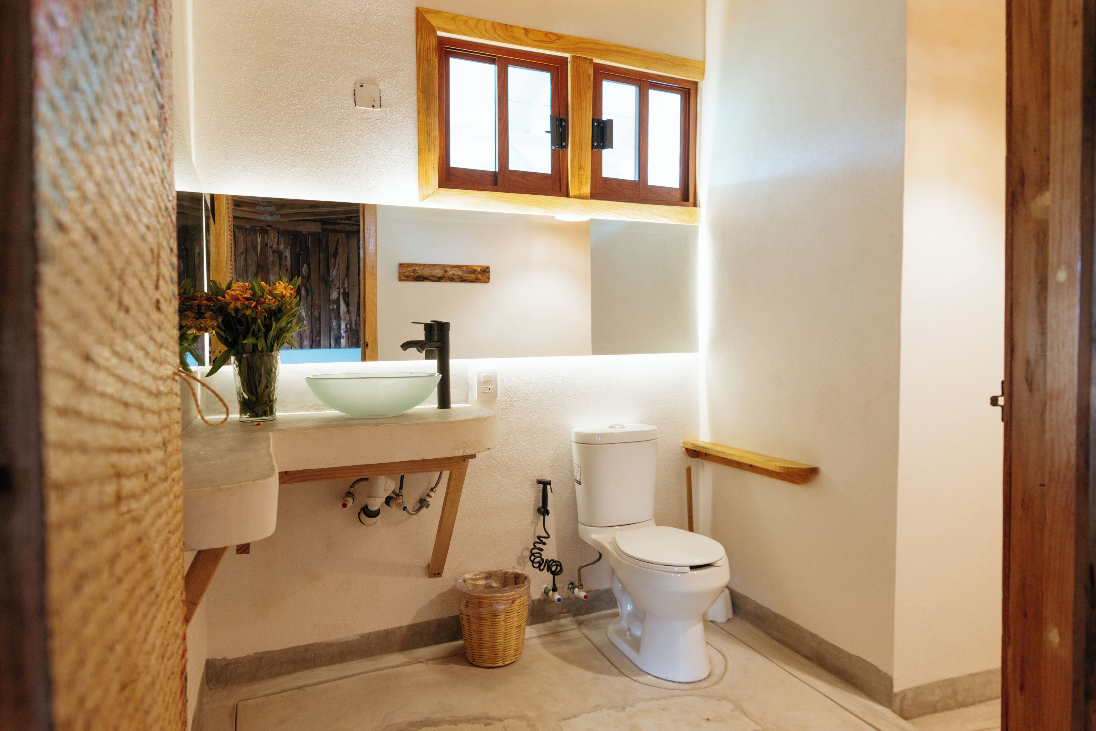 Ein Badezimmer mit einem Holzwaschtisch, einem weißen Waschbecken, einer Toilette und einem Korbwannenaufsatz auf dem Boden.