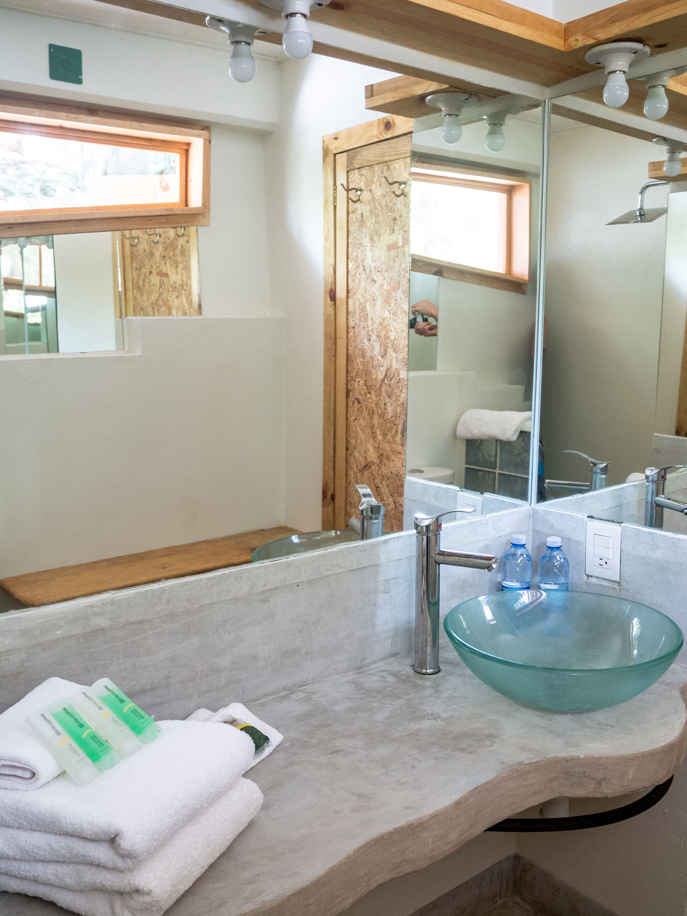 A bathroom with a glass sink, a wooden vanity, a mirror, and a window.
