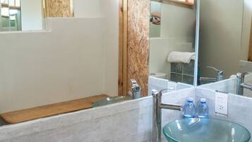 A bathroom with a glass sink, a wooden vanity, a mirror, and a window.