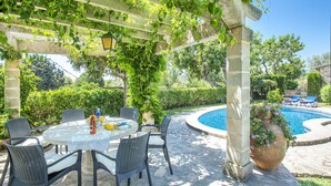 A covered outdoor dining area with a table and chairs, a pool, and surrounding greenery. - 3 Bedrooms, 2 bathrooms, enbeded into the natural mediterranean surrounding. (Pollença)