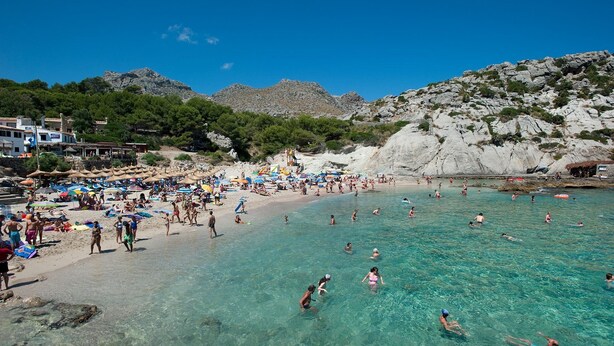 A beach with clear turquoise water, people swimming and sunbathing, and rocky hills in the background. - 3 Bedrooms, 2 bathrooms, enbeded into the natural mediterranean surrounding. (Pollença)