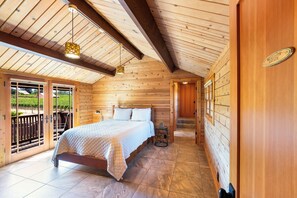 Ein Schlafzimmer einer Holzhütte mit einem Bett, einem kleinen Tisch und einem Fenster mit Blick auf einen Weinberg.