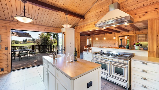 A modern kitchen with wooden walls, a large island, and a gas stove.
