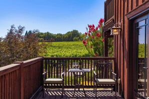 Eine Holzterrasse mit zwei Stühlen und einem Tisch, mit Blick auf einen Weinberg.