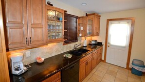Una cocina con armarios de madera, lavavajillas, cafetera y ventana con persianas.