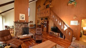 Amplia sala de estar con chimenea de piedra, sofás de cuero, una escalera de madera y una televisión.