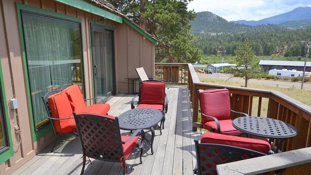 Una terraza con mobiliario exterior, incluyendo sillas y mesas, ofrece vistas a un paisaje pintoresco con montañas y árboles.