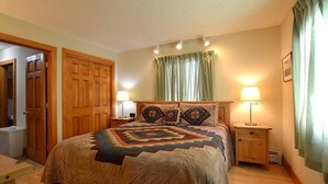 Un dormitorio con una cama grande, dos mesitas de noche con lámparas, un armario de madera y una ventana con cortinas.