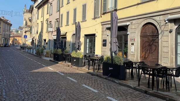 A cobblestone street lined with yellow buildings, outdoor seating, and a clear blue sky. - Little Suite Bergamo (Bergamo)