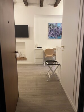 A modern room with a wooden floor, a desk with a chair, a flat-screen TV mounted on the wall, and a painting above the desk. - Little Bergamo Suite (Bergamo)
