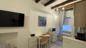 A compact kitchen with a dining area, a flat-screen TV mounted on the wall, a microwave, and a small refrigerator. - Little Suite Bergamo (Bergamo)