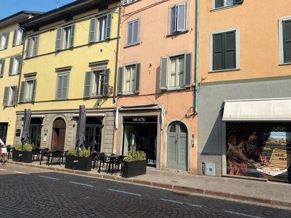 A street with buildings, outdoor seating, and a shop with a sign. - Little Bergamo Suite (Bergamo)