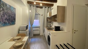 A compact kitchen with a washing machine, a dining area with a table set for two, and a large window with curtains. - Little Suite Bergamo (Bergamo)