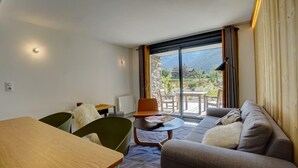 A modern hotel room with a dining area, a sofa, and a balcony with a view of the mountains.