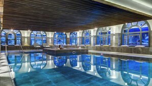 A large indoor swimming pool with arched windows and a wooden ceiling.