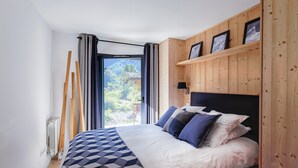 A bedroom with a bed, wooden paneling, a view through a window, and a door.