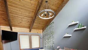 A bedroom with a large bed, a blue sofa, a TV mounted on the wall, and a wooden ceiling. - TRI-LEVEL HOUSE WITH HUGE DECK AND AMAZING VIEWS OF THE BLACK HILLS (Custer)