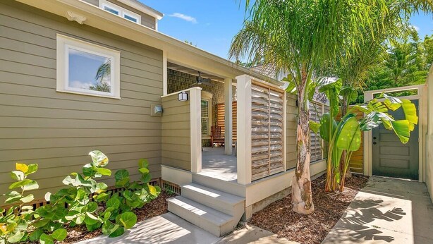 Une maison moderne dotée d’un porche abrité, d’un petit jardin planté de plantes tropicales et surplombant un ciel dégagé.