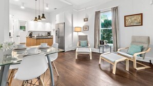 Une cuisine moderne avec des armoires blanches, un four encastré et un réfrigérateur en acier inoxydable. On y trouve également un coin repas avec une table en verre et des chaises blanches.