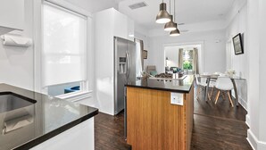 Une cuisine moderne dotée d’un îlot central, d’appareils électroménagers en acier inoxydable et d’un coin repas avec une table et des chaises en verre.