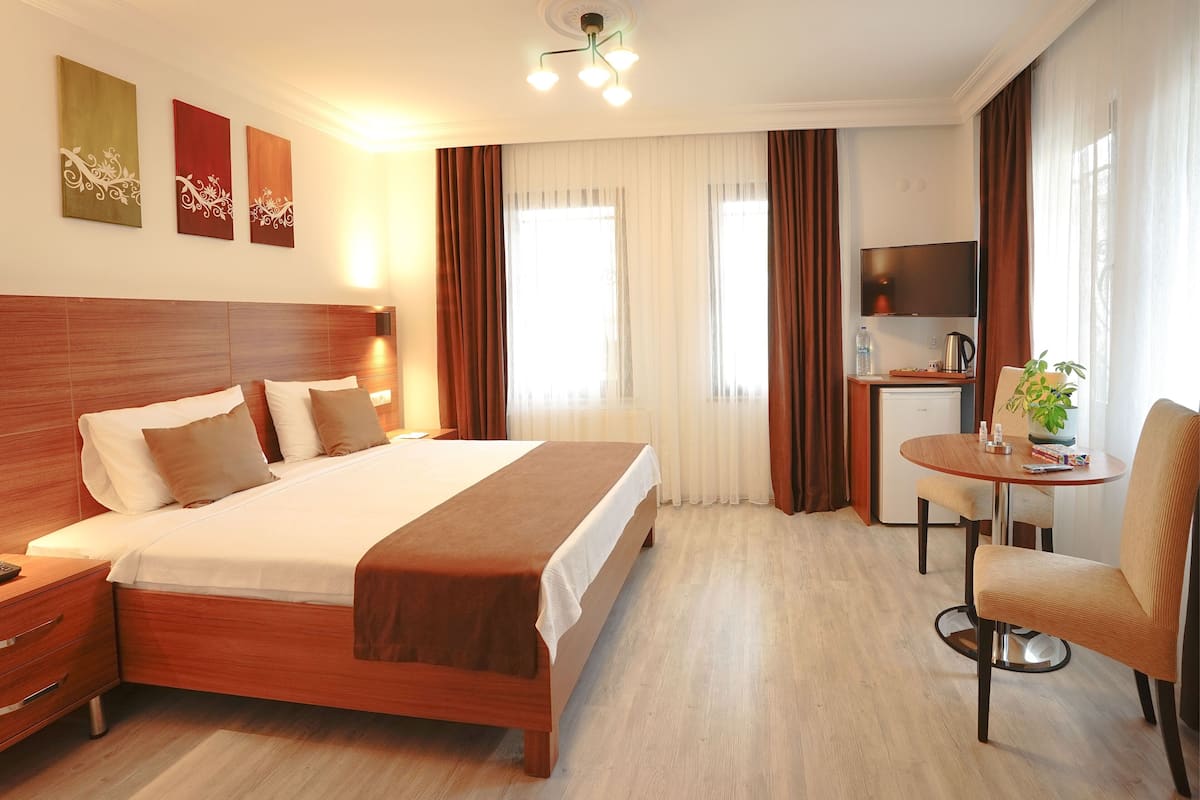 A hotel room with a wooden bed, a desk with a chair, a TV, and a window with curtains.