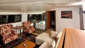 Un salón moderno con un sofá, sillones, una mesa de centro y una mesa de madera. Se ve una ventana con vistas a la ciudad de noche.