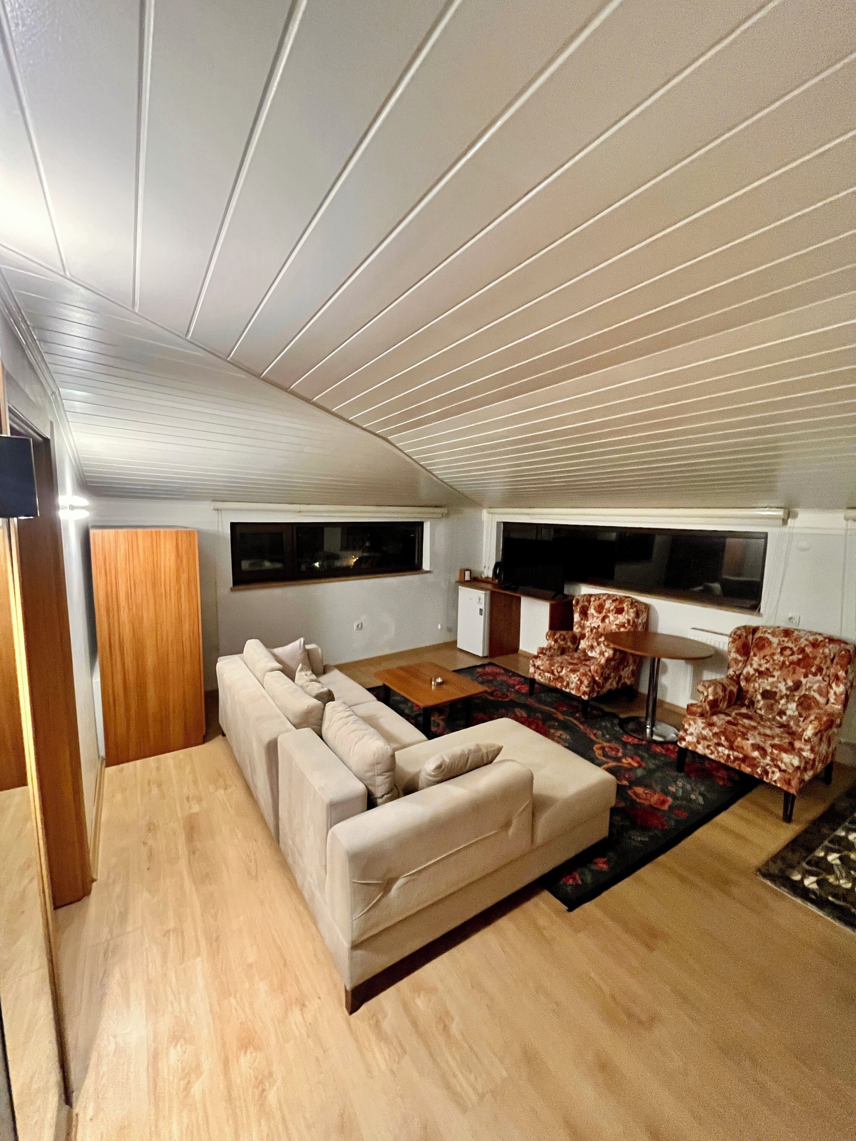 A compact living space with a sofa, two patterned armchairs, a small table, and a television.