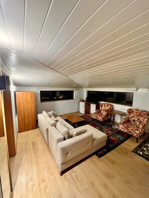 Un espacio habitable compacto con un sofá, dos sillones estampados, una mesita y un televisor.
