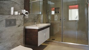 Un bany modern amb paret de marbre, vàter blanc, rentapel i una cabina de dutxa de vidre.
