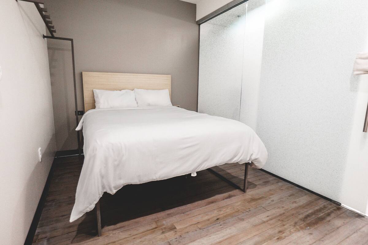 A bedroom with a wooden bed frame, white bedding, and a wooden floor.