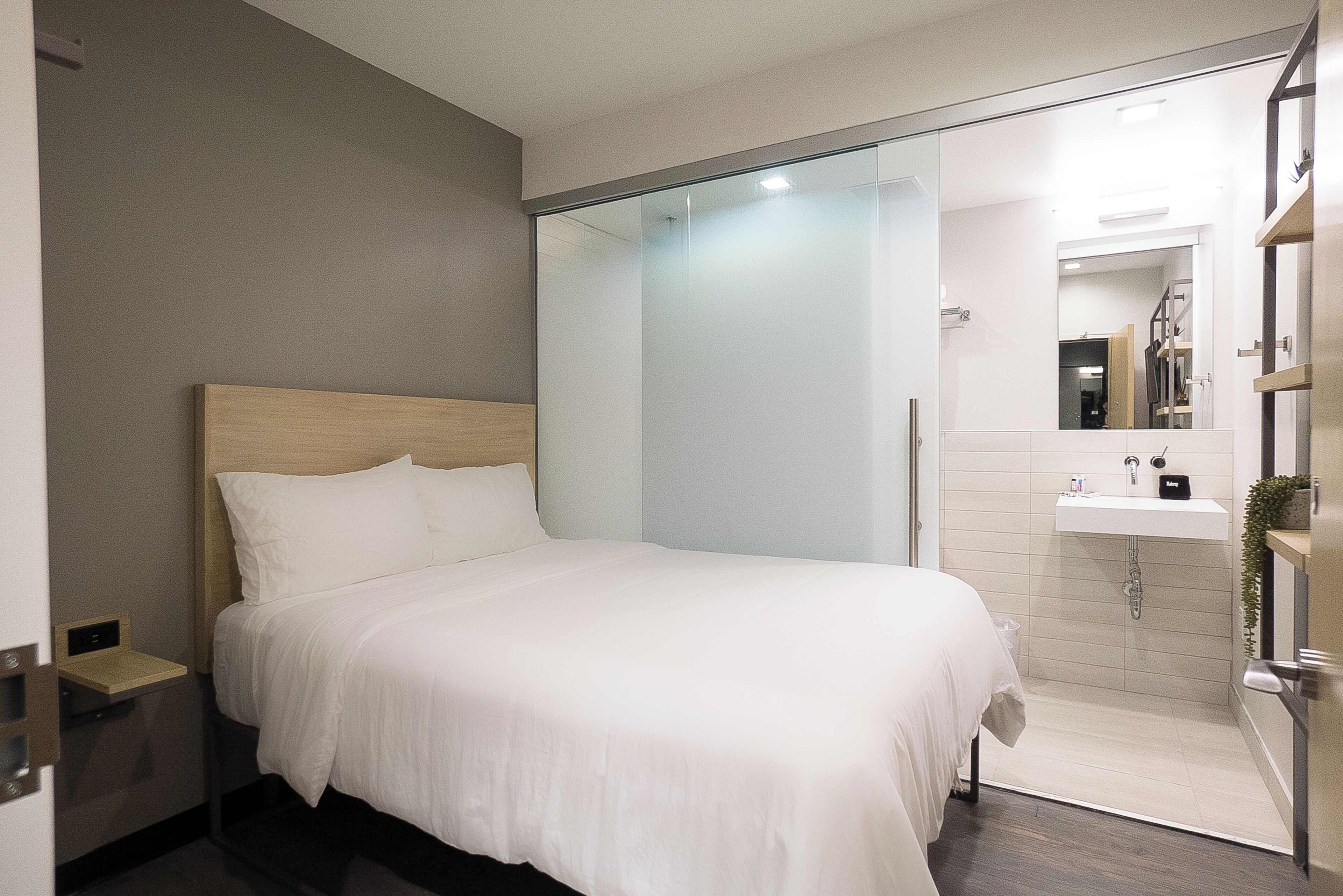Une chambre d’hôtel moderne dotée d’un grand lit, d’une douche à parois de verre, d’une petite table de chevet et d’un lavabo intégré.