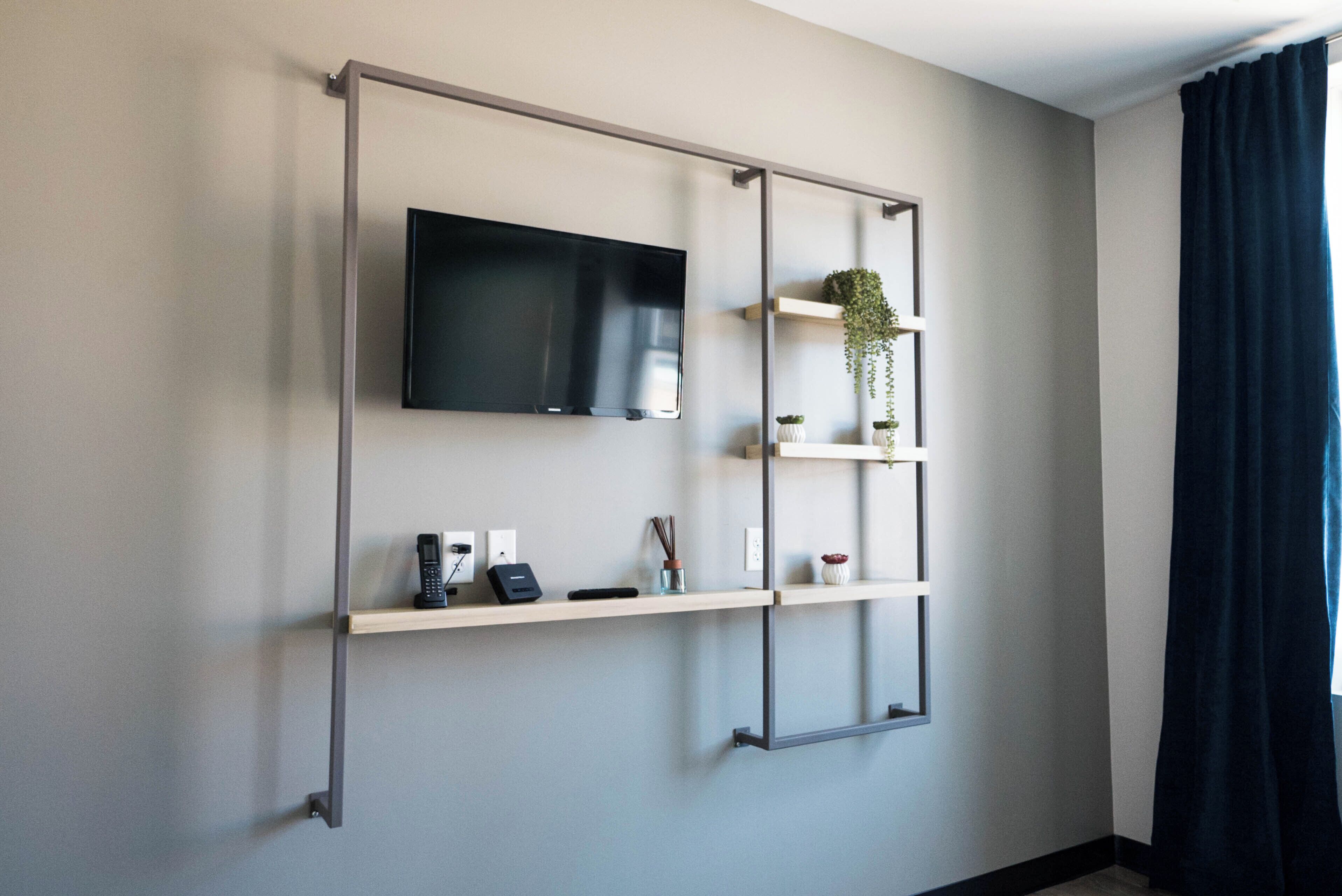 A modern living room with a mounted TV, two shelves with decorative items, and a dark curtain.