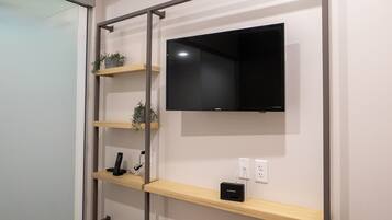 A wall-mounted TV with a shelf below it, holding a remote control and a small device.