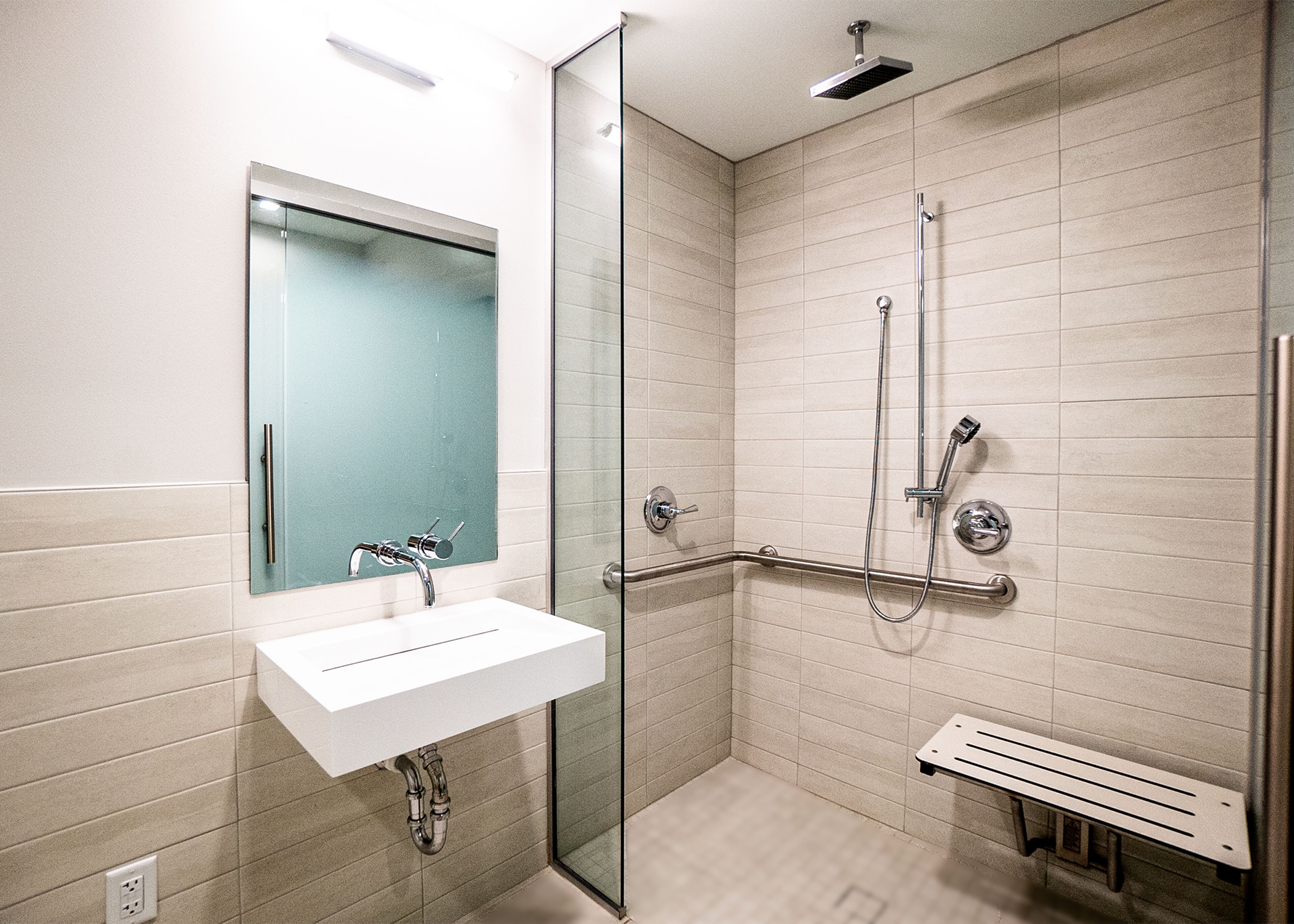 A modern bathroom with a glass shower enclosure, a white sink, and a bench.