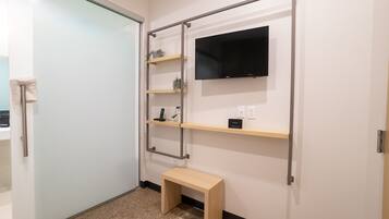 A bathroom with a glass door, a wooden bench, and a wall-mounted TV.