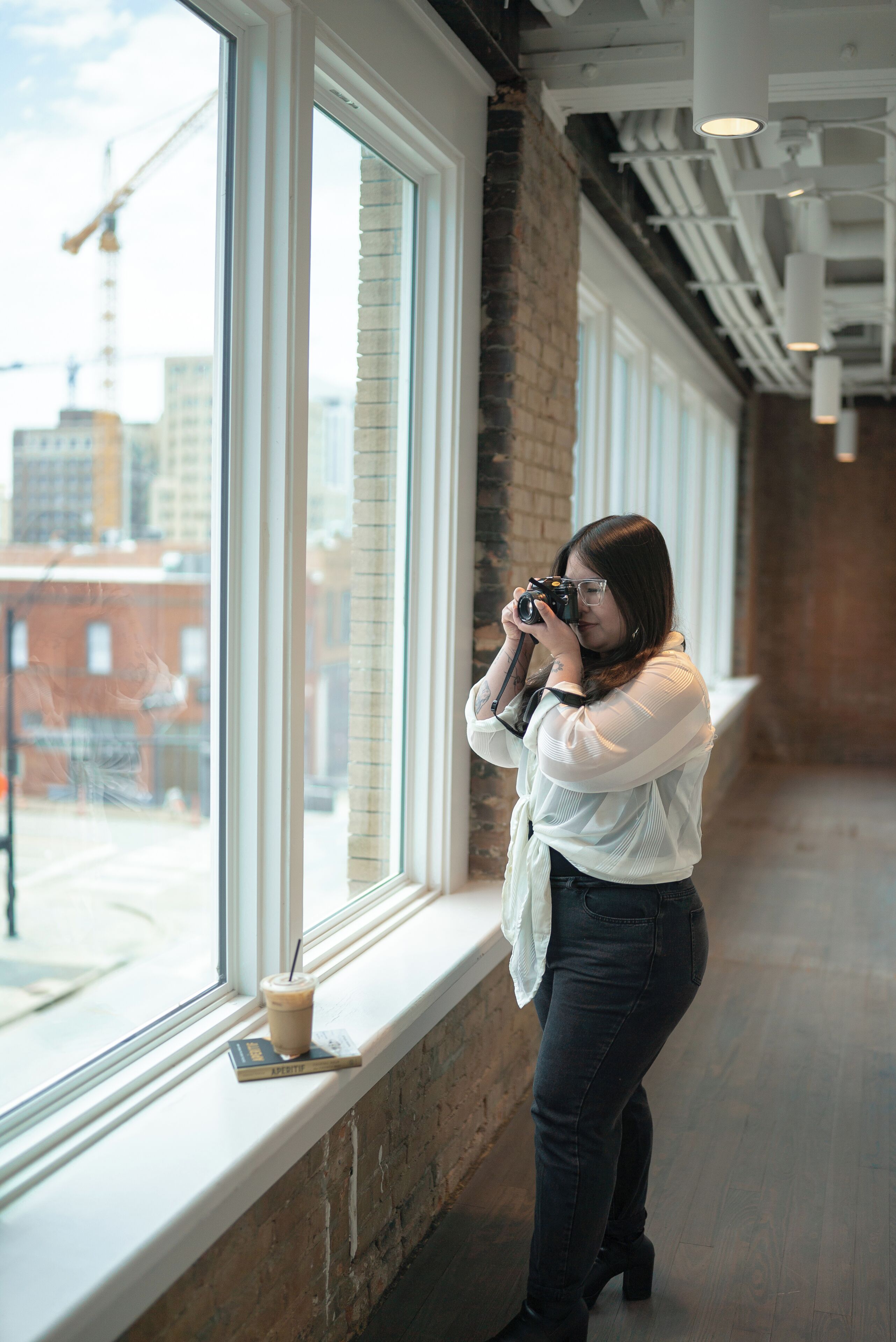 A person taking a photo through a window with a view of buildings and a construction crane outside.