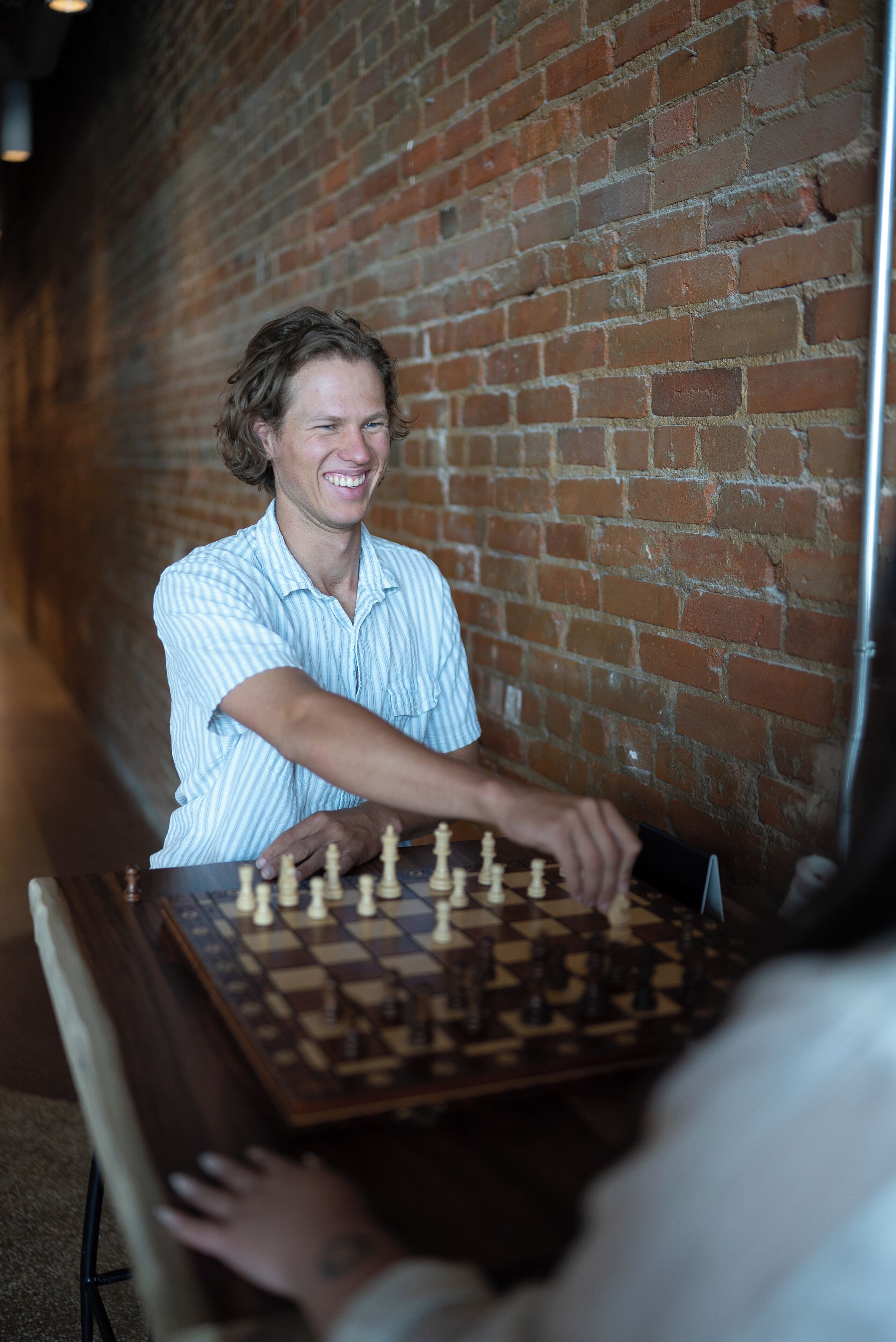 A person playing chess at a table with a brick wall in the background.