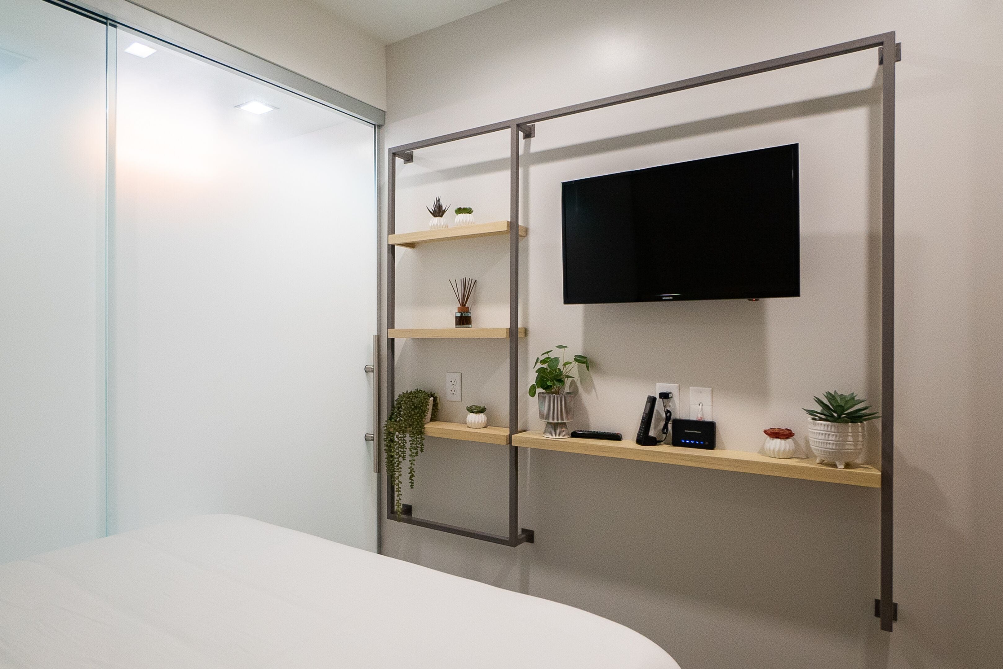 Una camera da letto moderna con un letto, una TV a parete e mensole con oggetti decorativi.