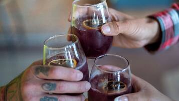 Three hands holding glasses of a dark beverage, likely wine, with visible tattoos on the hands.